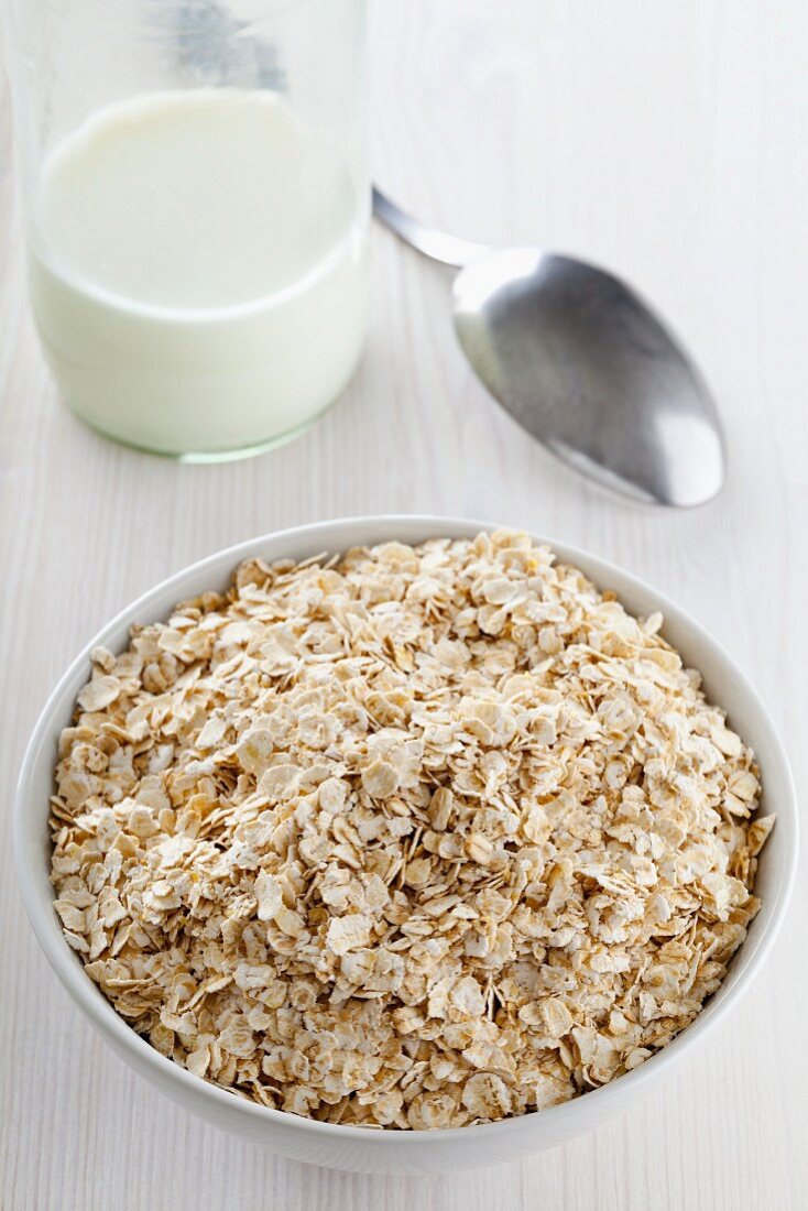 A bowl of oats in front of a bottle of milk
