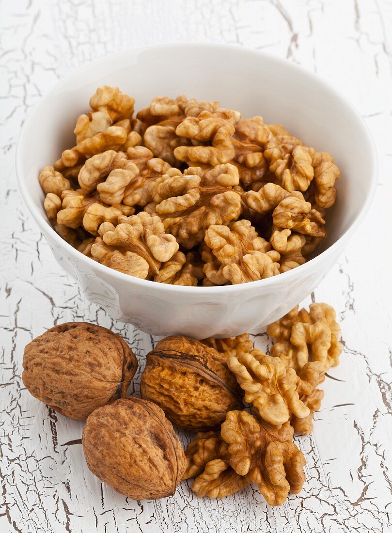 A bowl of walnuts with a whole nuts and shelled nuts in front of it