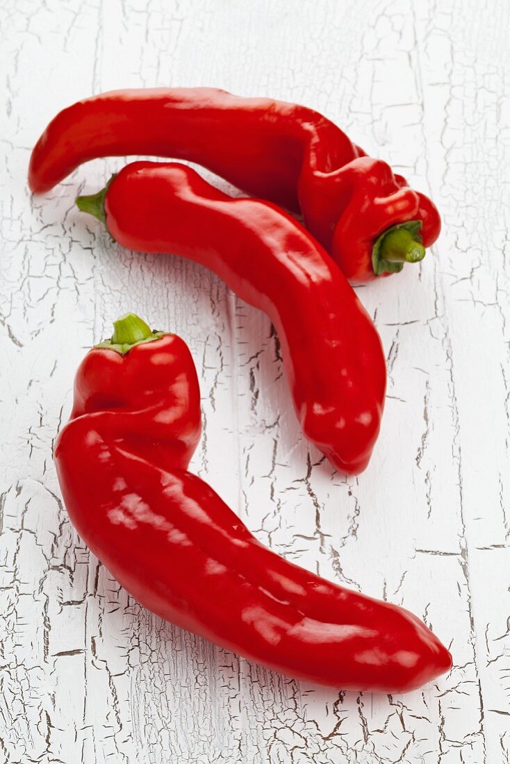 Three red pointed peppers on a white wooden table