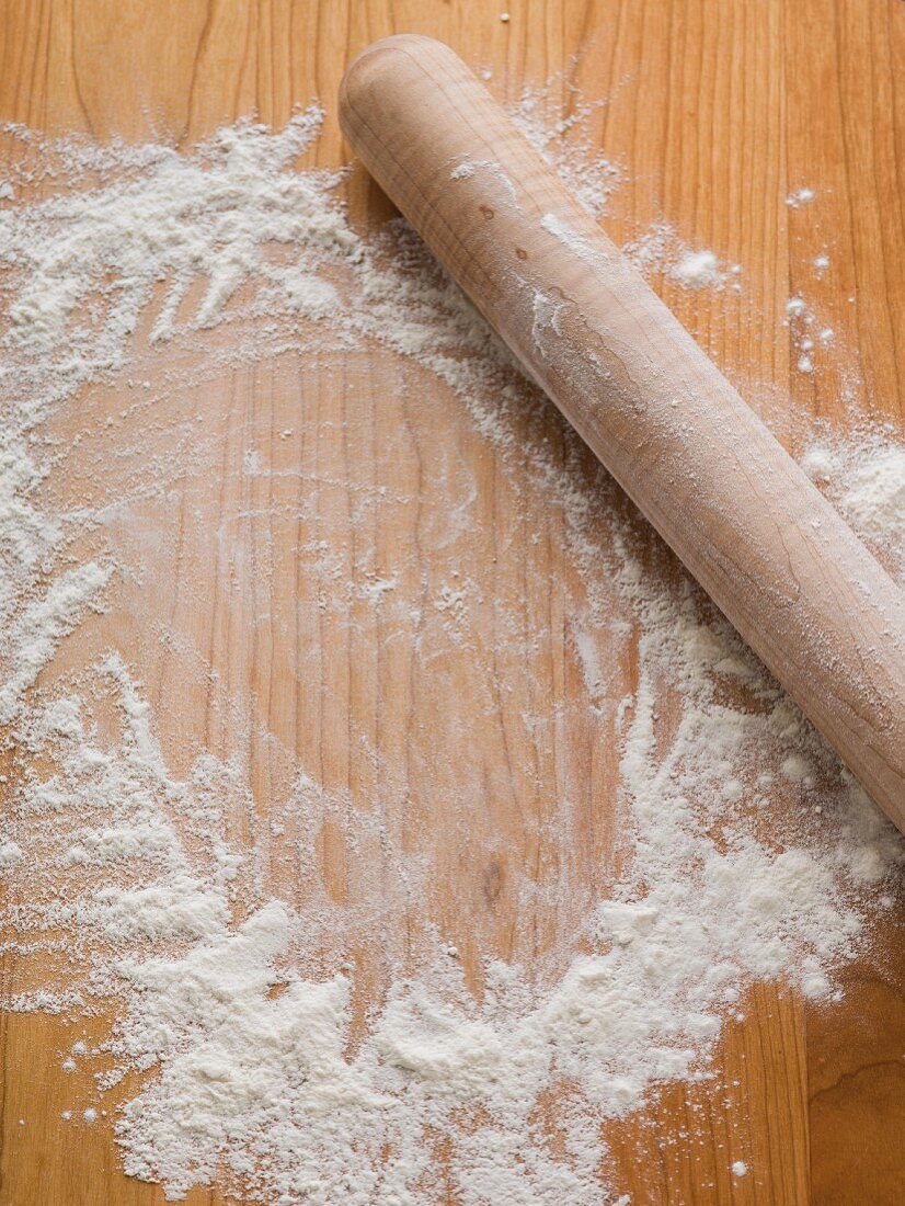 Flour sprinkled on a wood surface woth a rolling pin