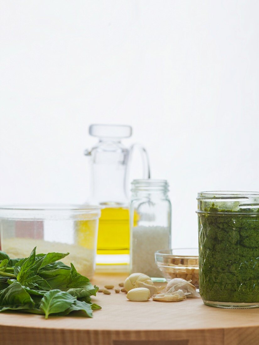 Pesto in a jar with individual ingredients of basil, garlic, pine nuts, romano cheese, sea salt and olive oil