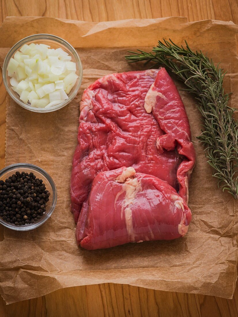 Frisches Steak auf braunem Papier mit Rosmarin, Zwiebeln und schwarzen Pfefferkörnern