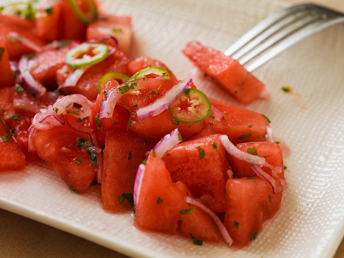 Close-up of watermelon salad with onions and serrano peppers on a rectangular plate with a linen texture