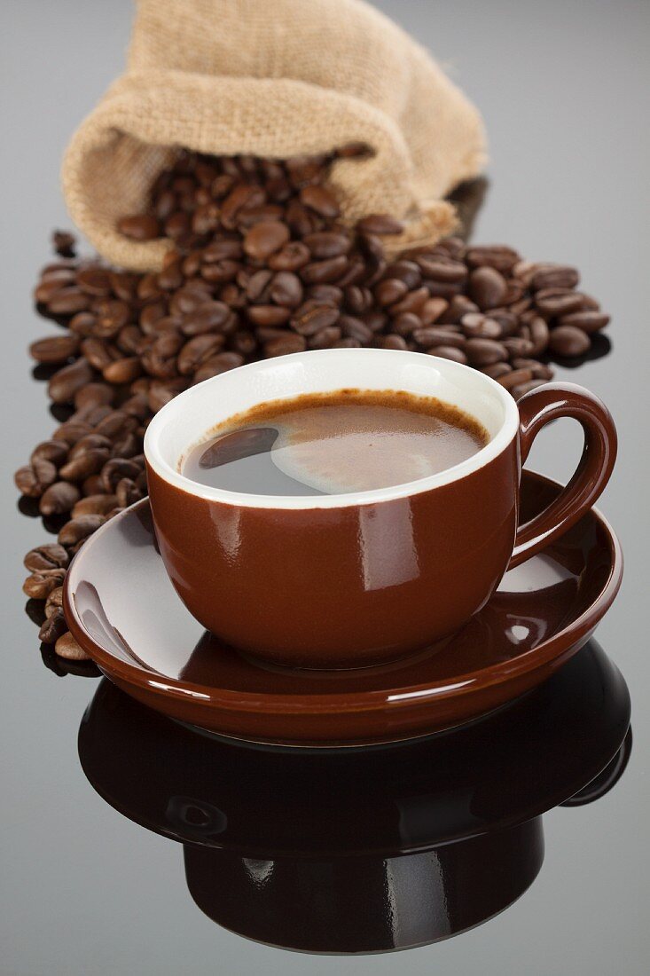 An espresso in a brown cup in front of a sack of coffee beans