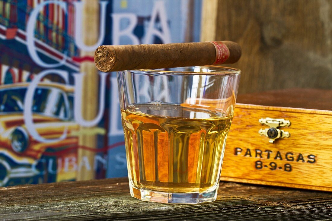 A Cuban cigar balanced on a glass of rum