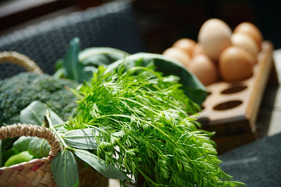 A basket of garden vegetables with fresh chicken's eggs in the background