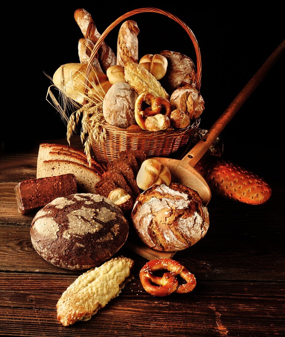 Various types of bread and rolls in a basket with ears of wheat