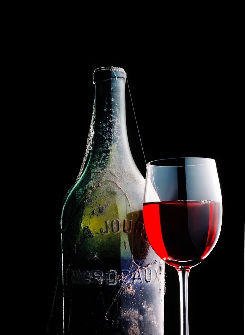 Rotweinglas neben einer alten Weinflasche mit Spinnweben
