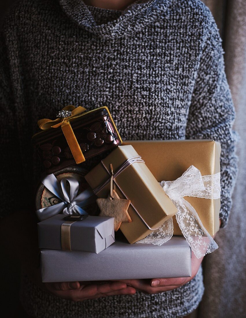 Frau mit schwarzweiss meliertem Pullover trägt einen Stapel Geschenkpäckchen