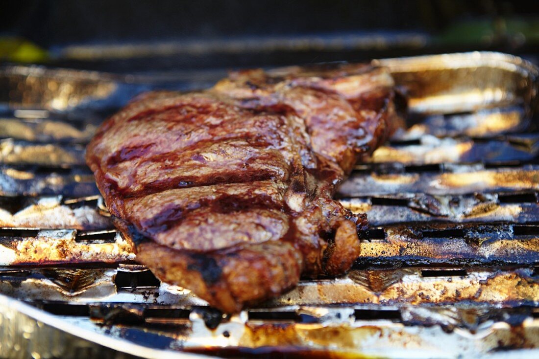 A T-bone steak in an aluminium tray on a barbecue (close-up)