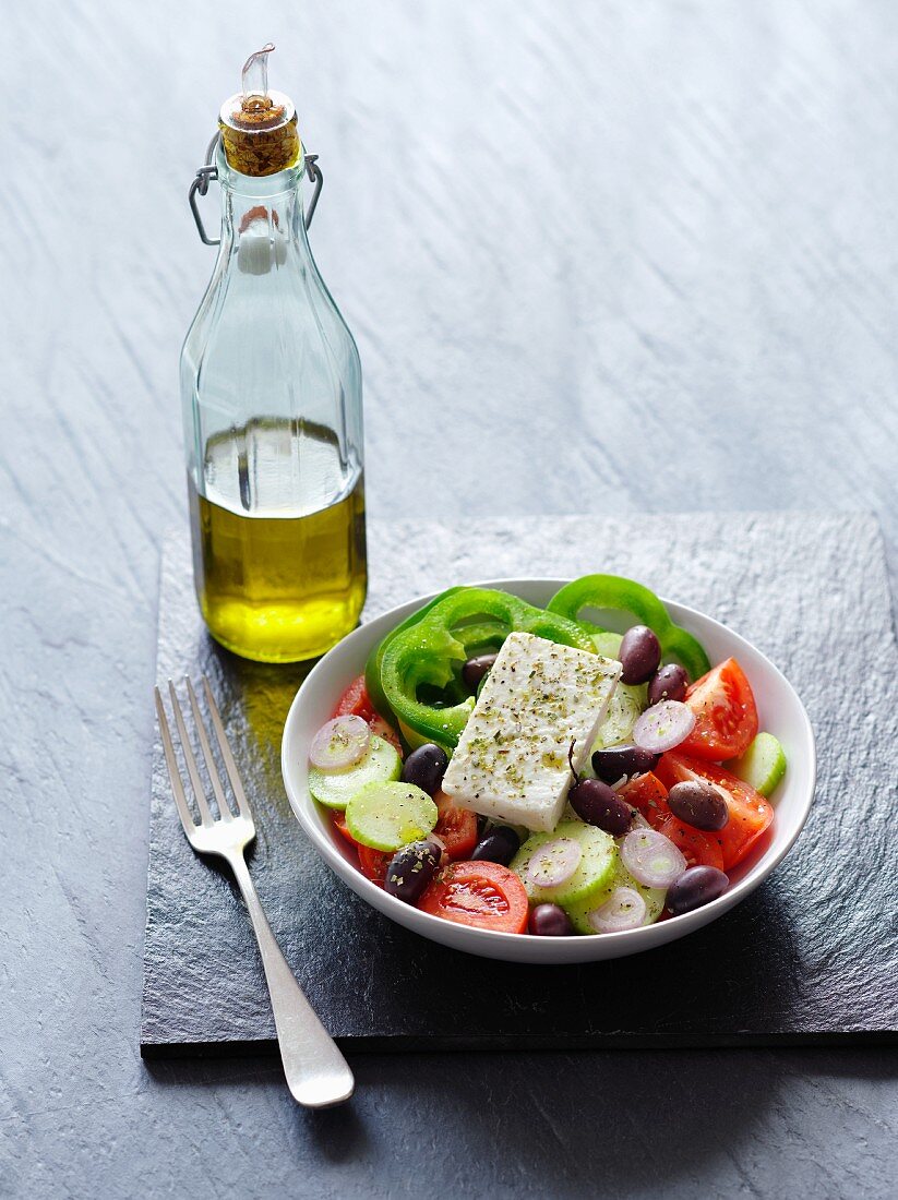 Griechischer Salat, daneben eine Flasche mit Olivenöl