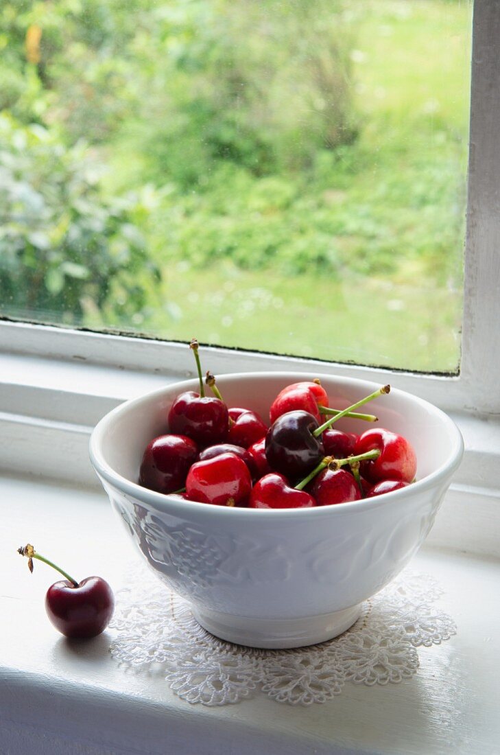 A bowl of fresh cherries on a windowsill