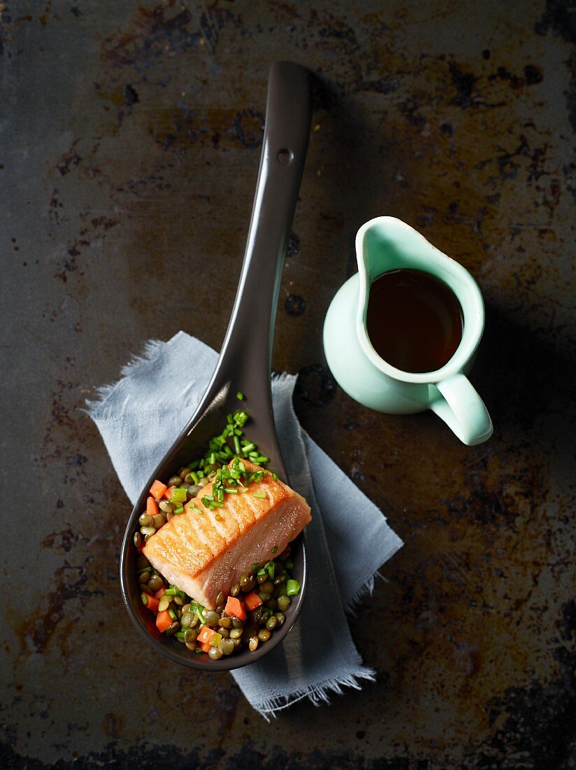 Salmon fillet with lentils on a spoon next to a little jug of soy sauce