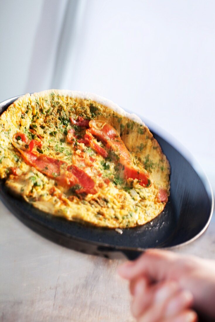 A hand holding a bacon pancake in a pan