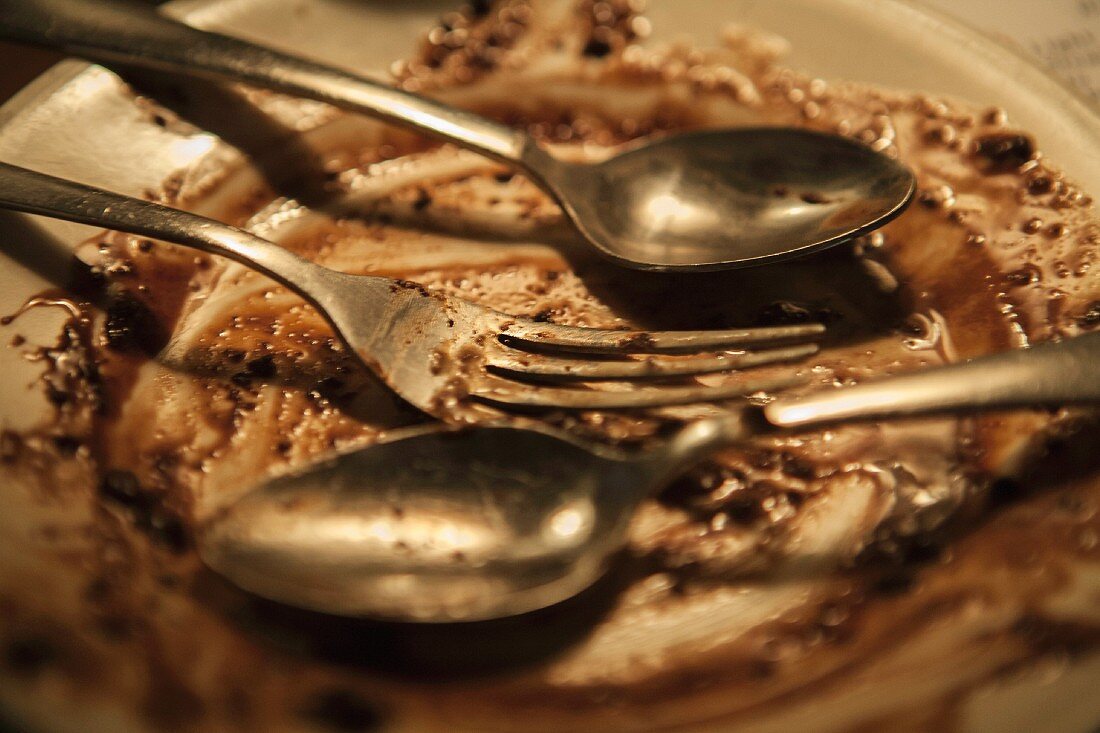 The remains of a chocolate dessert on a plate with two spoons and a fork