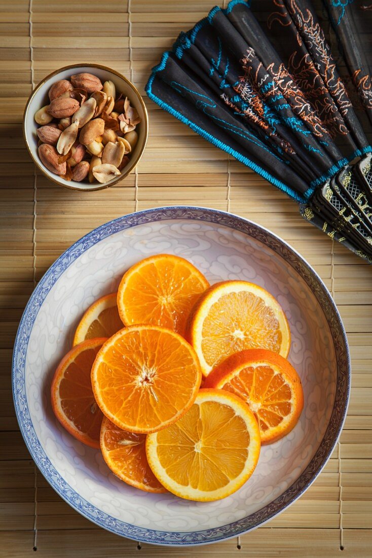 Orangenscheiben auf Teller, daneben Schälchen mit Erdnüssen