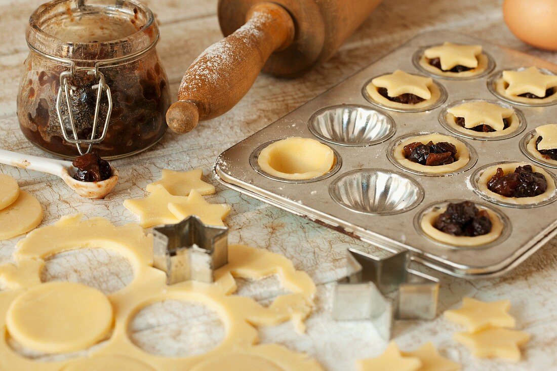 Mini mince pies being decorated with star-shaped lids in the baking tin