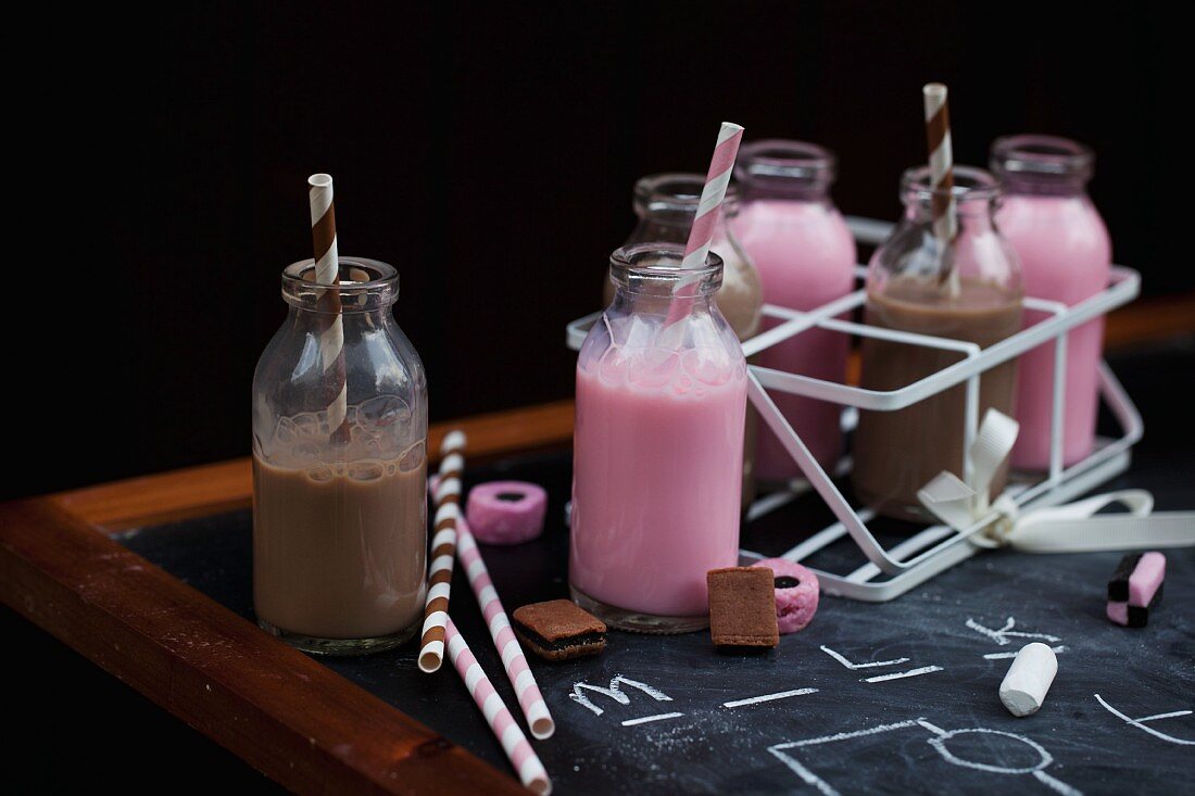 Chocolate milk and raspberry milk in mini bottles with liquorice sweets on a chalkboard