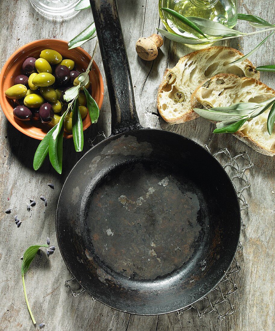 Leere Pfanne, Salbei, schwarze und grüne Oliven, Olivenöl, Olivenzweig, Oliven-Ciabatta und Lavendel