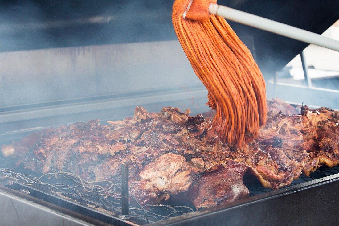 Barbecued meats being moistened with a mop