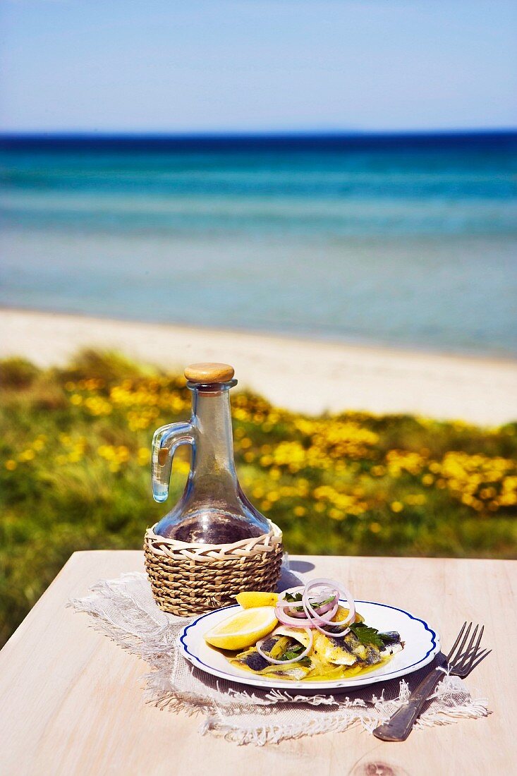 Sardinen mit Olivenöl & Zitronen auf Tisch am Meer