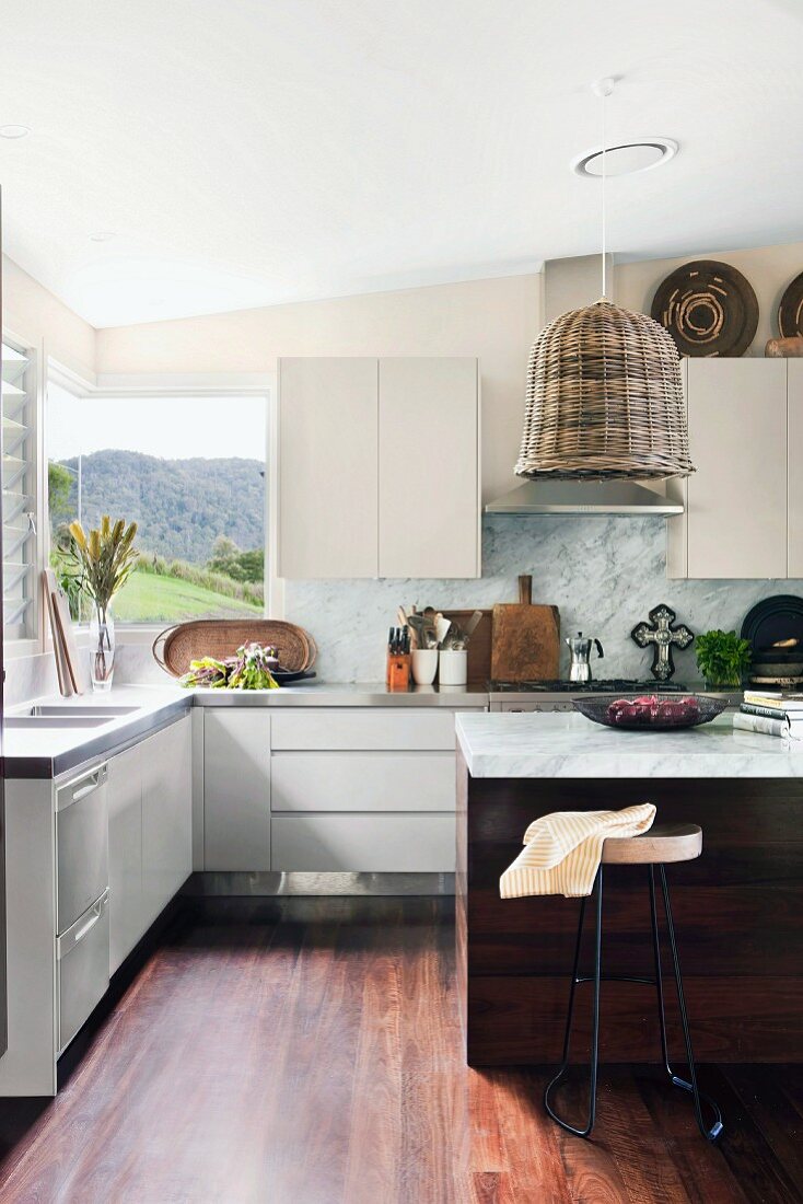 weiße Einbauküche mit Panorama-Eckfenster und Korblampe über Küchentheke, verschiedene Küchenutensilien auf Edelstahl-Küchenarbeitsplatte arrangiert