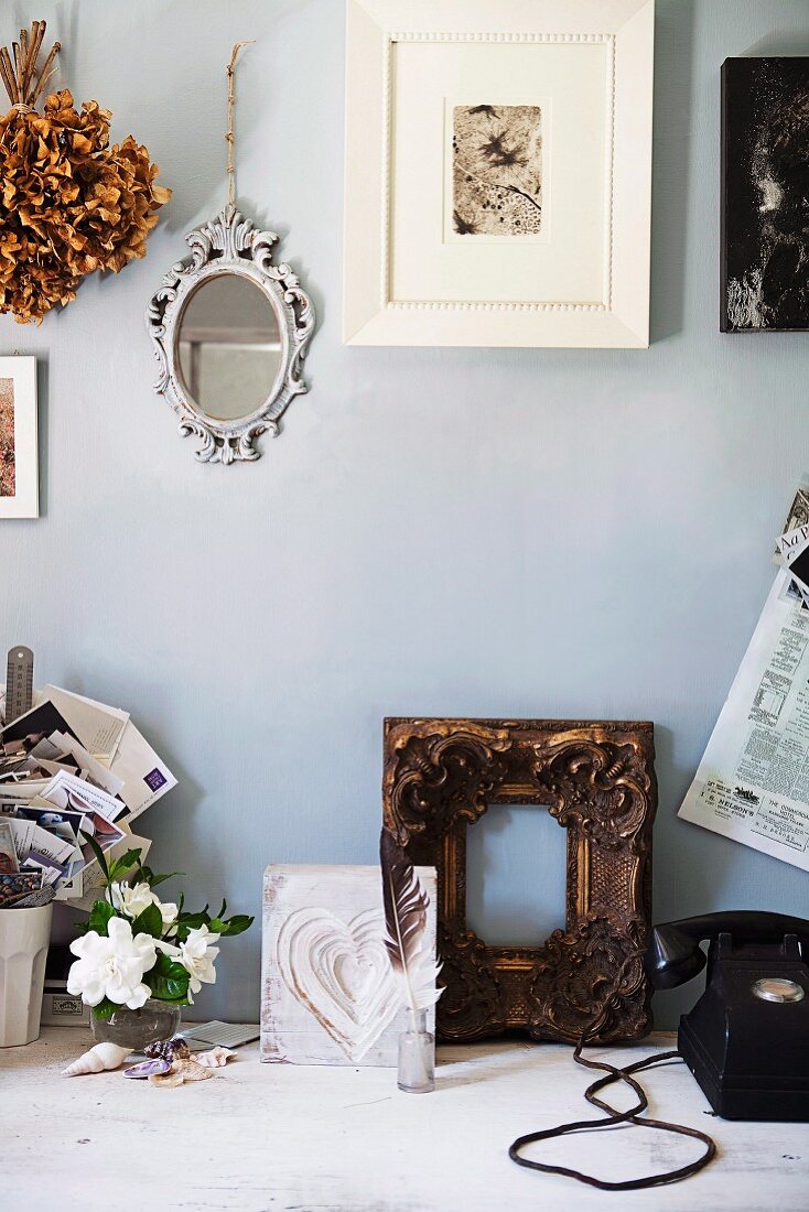 Photo in white frame and mirror on wall above gilt wooden frame and various vintage items on rustic wooden table