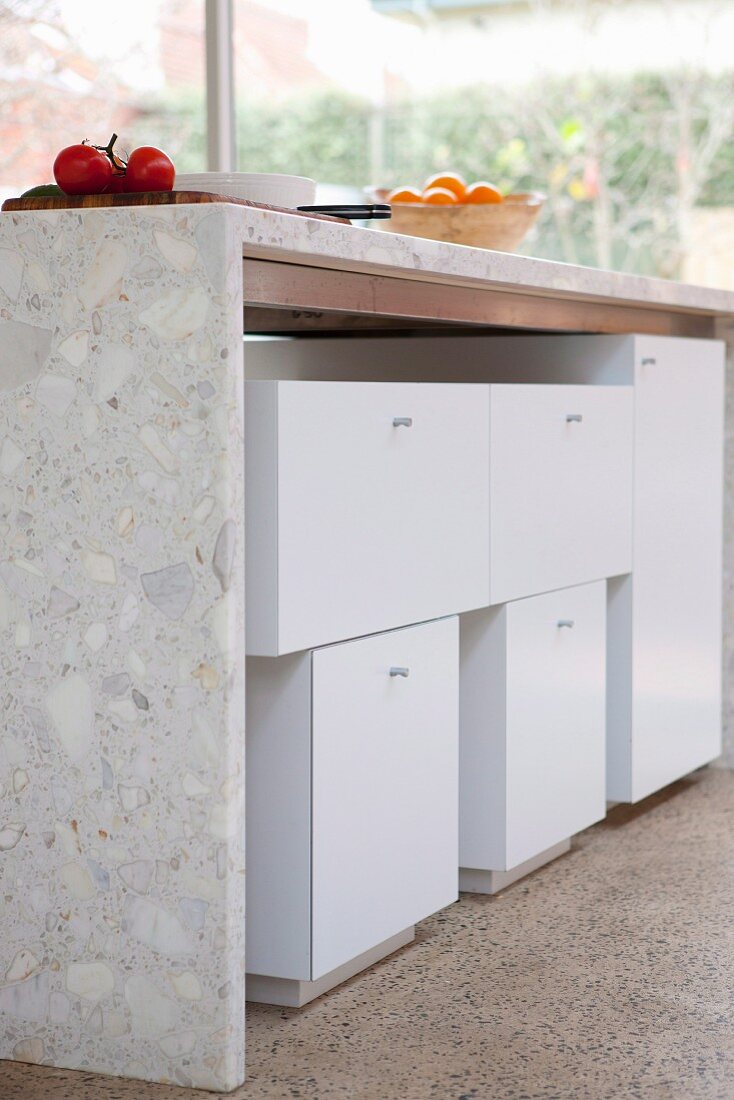 Fruit on concrete composite kitchen counter with white cabinet modules below on terrazzo floor