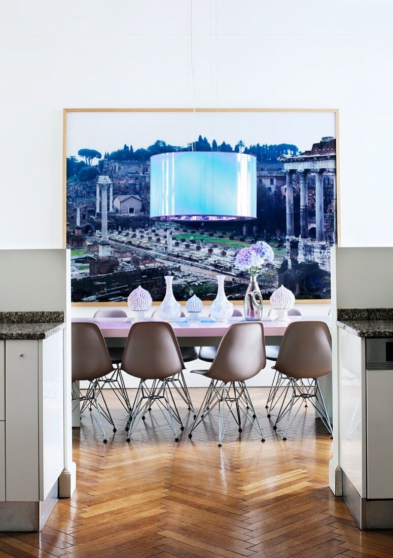 View between kitchen base units through doorway to dining area with Eames chairs and designer lamp in front of large photo of the Roman Forum