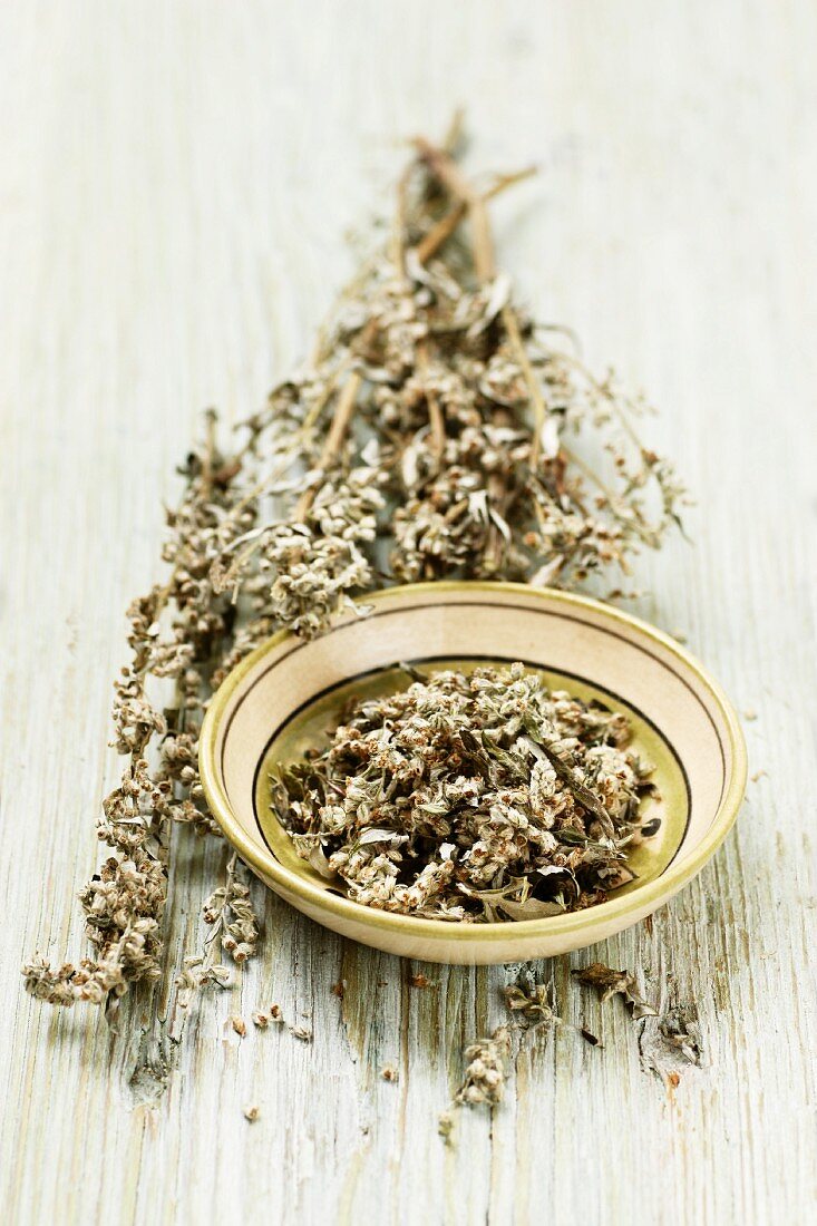 Mugwort with flowers in a bowl and on a wooden surface