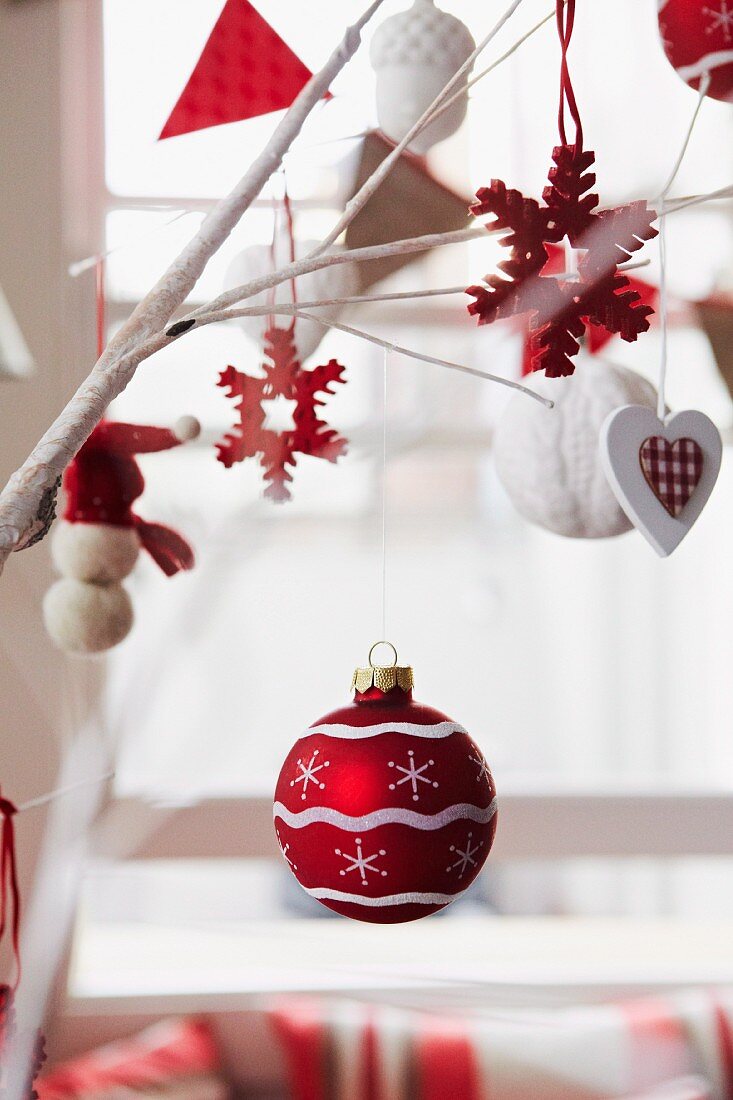 Rot-weisser Weihnachtsschmuck an Zweigen aufgehängt vor Fenster im Hintergrund