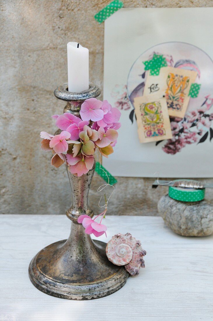 Hortensienblüten an Silberdraht und Muschelschnecke als Schmuck für patinierten Kerzenständer; nostalgische Collage im Hintergrund