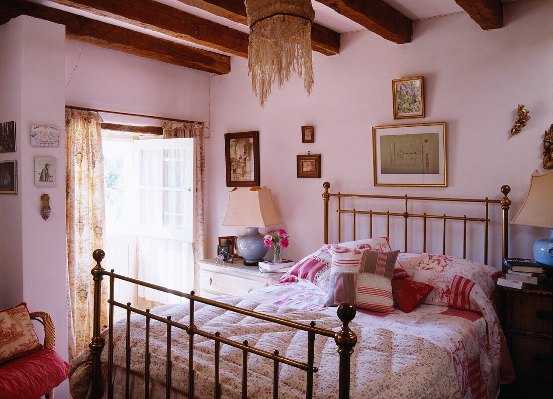 Hand-sewn quilts and scatter cushions on brass bed in romantic bedroom of historical farmhouse
