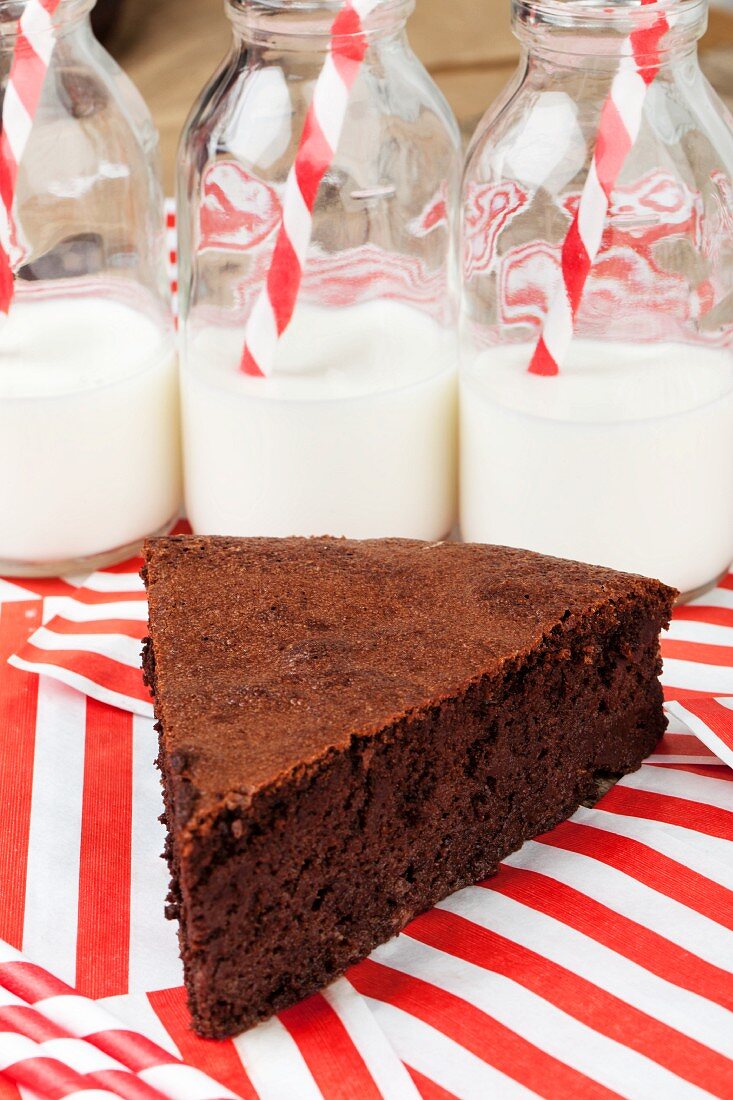 Slice of chocolate cake in front of bottles of milk