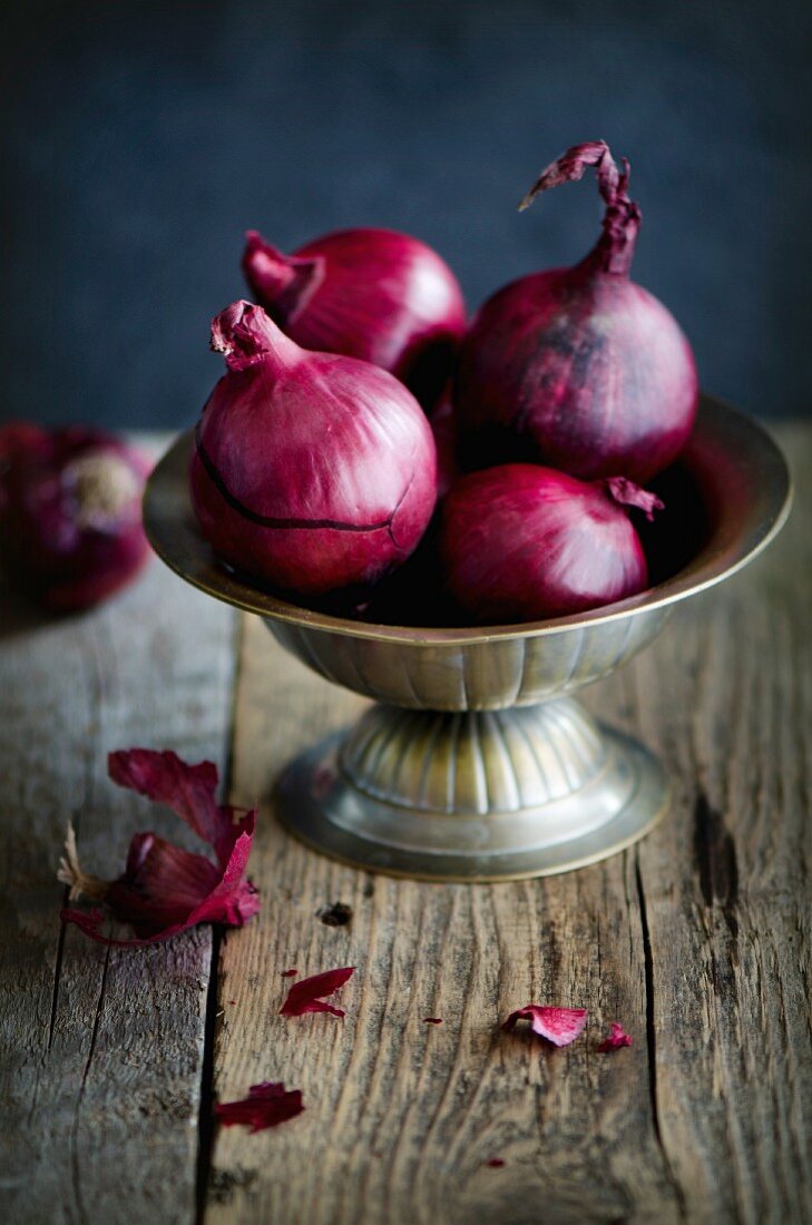 Red onions in a metal bowl on a wooden surface