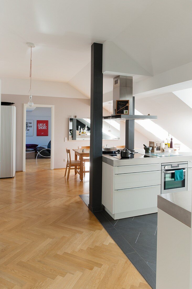 Converted attic interior with kitchen area on grey tiled floor and dining area with wooden herringbone floor