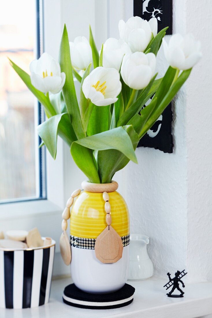 weiße Tulpen in Vase mit Holzperlenkette dekoriert auf Fensterbank