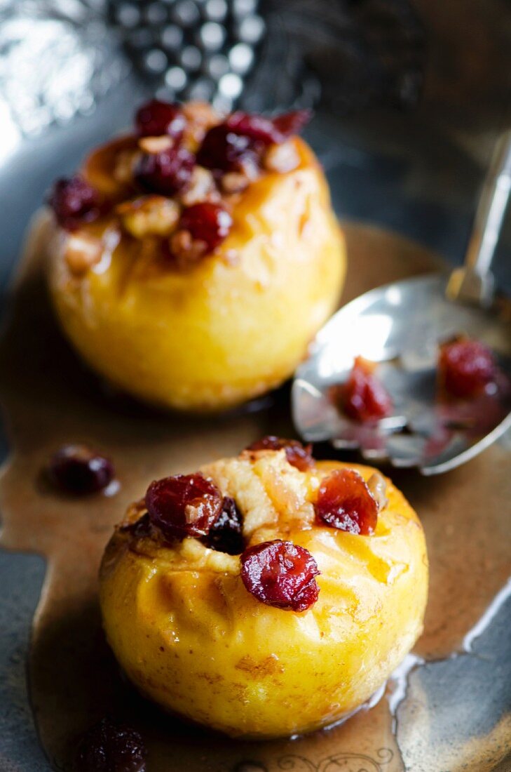 Two baked apples with cranberries on a pewter dish with a silver spoon