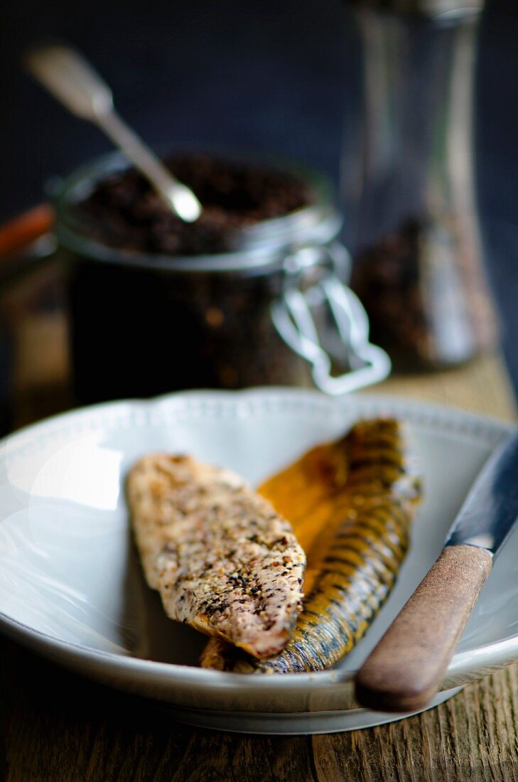 Smoked peppered mackerel fillets in front of a jar of peppercorns