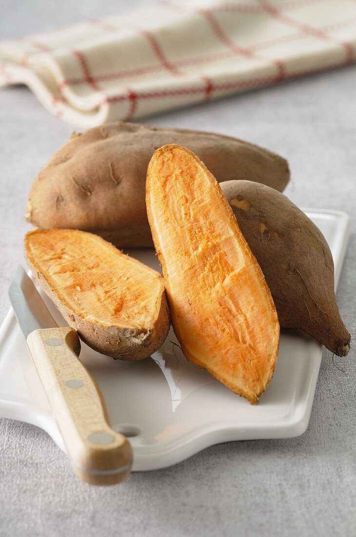 Sweet potatoes, whole and halved, on a chopping board