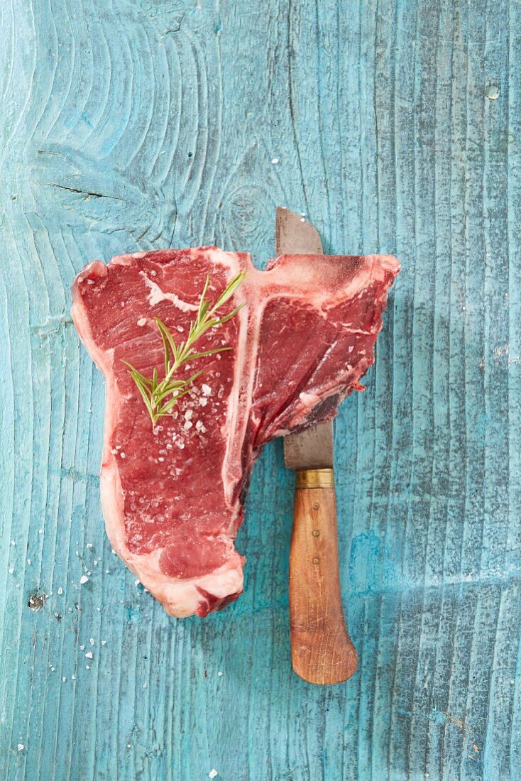 Raw T-bone steak with salt and rosemary on a knife