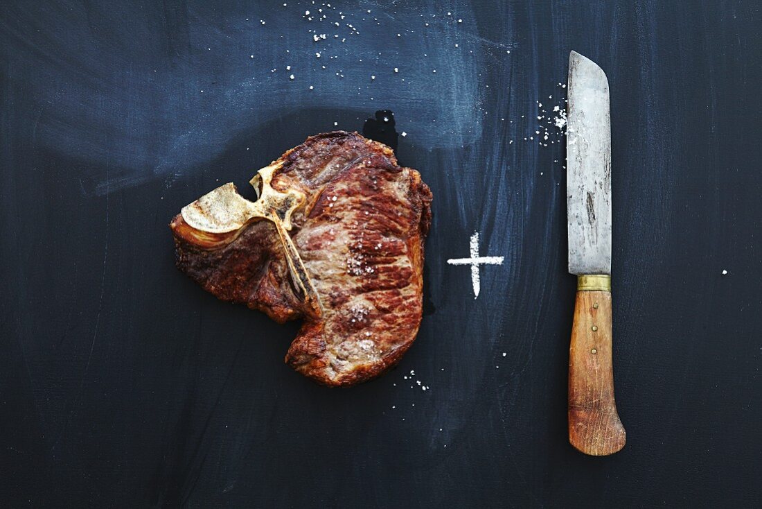 A fried T-bone steak and a knife on a chalkboard