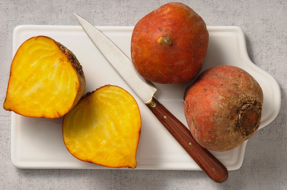 Yellow beets, whole and halved, on a chopping board with a knife