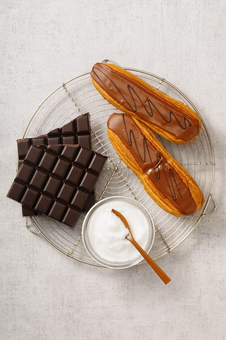 Chocolate eclairs, a bar of chocolate and sugar on a wire rack