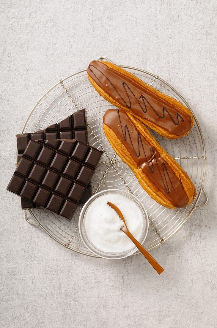 Eclairs mit Schokoladenglasur, Schokoladentafel und Zucker auf Kuchengitter