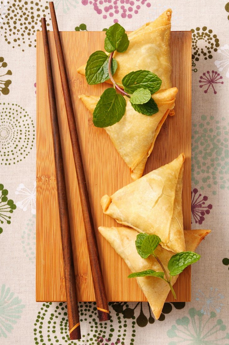 Samosas, fresh mint and chopsticks on a wooden board