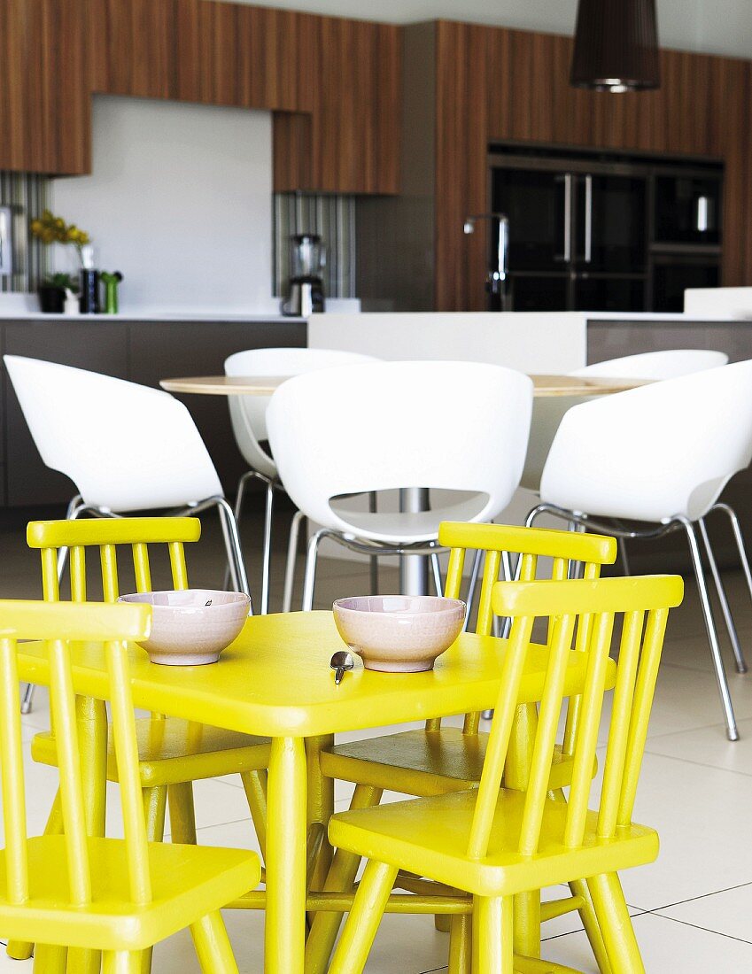 Yellow children's table and chairs in front of modern, white shell chairs in open-plan kitchen