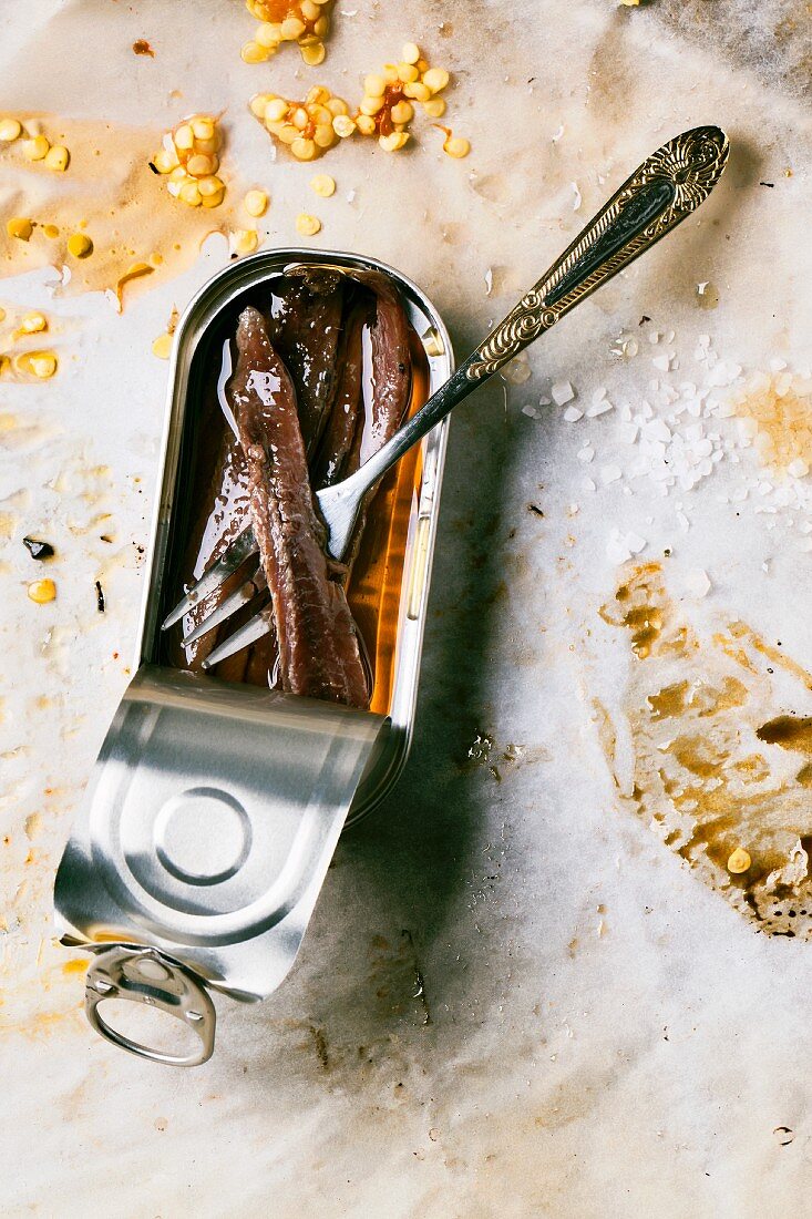 An open can of anchovies on dirty baking paper