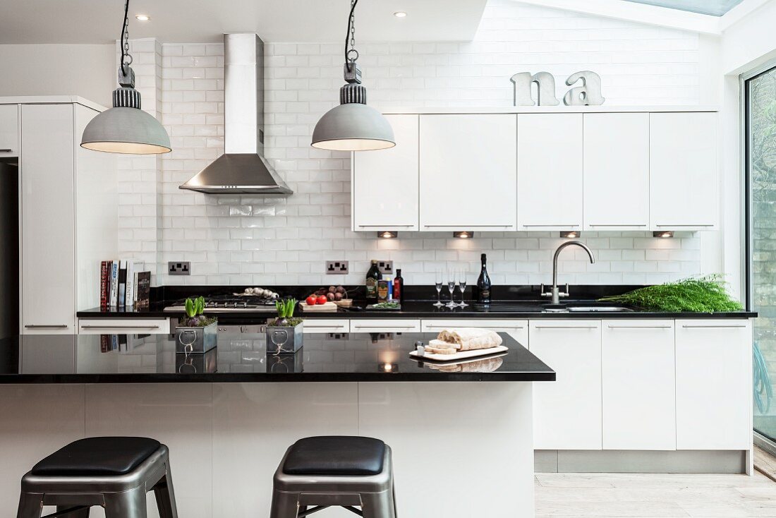 Island counter with black, glossy worksurface in open-plan designer fitted kitchen with white fronts