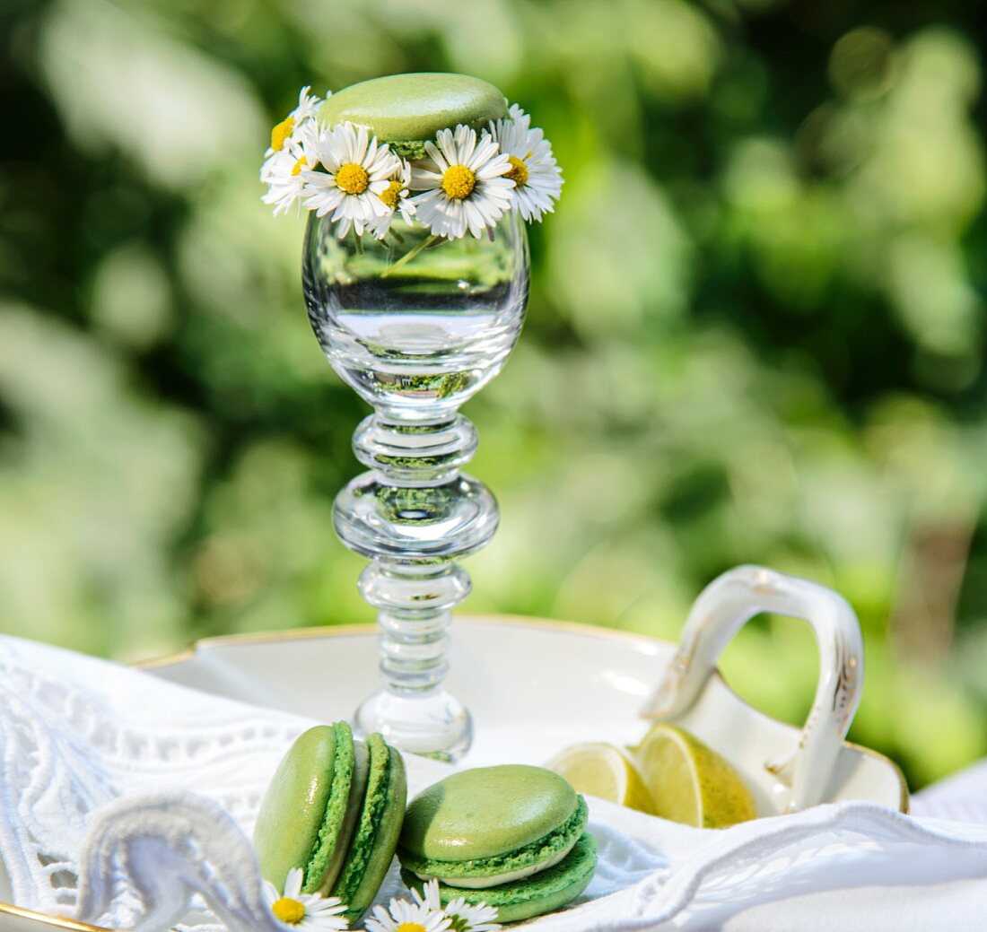 Grüne Macarons mit Gänseblümchen und Glas auf Gartentisch